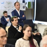 The audience pictured during a presentation, with organizer Rustam Kagirov pictured in the background. Photo: Skoltech.