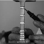 CNT-nanocomposites being tested for piezoresistive response in an Intron 5969 Universal Testing Systems under tensile load. The values of resistance change as increasing tensile load is applied which allow the material to send a self-report as to its condition. The silver lines are conductive contacts and the white speckles are used by the LIMESS digital image correlation (DIC) system to calculate strain values. Image was taken in the Laboratory of Mechanical Testing, CDMM.